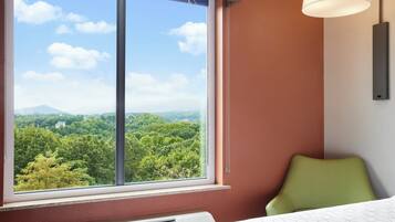 A hotel room with a large window offering a view of a forested landscape.