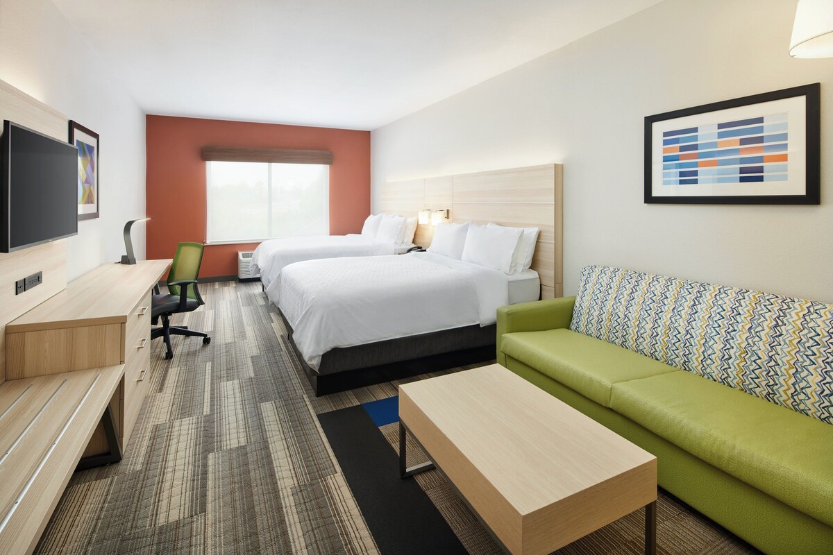Ein Hotelzimmer mit Bett, Schreibtisch, grünem Sofa, Fernseher und Fenster.