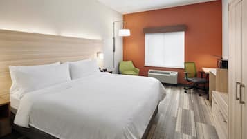A hotel room with a large bed, a desk with a chair, a lamp, and a window with blinds.
