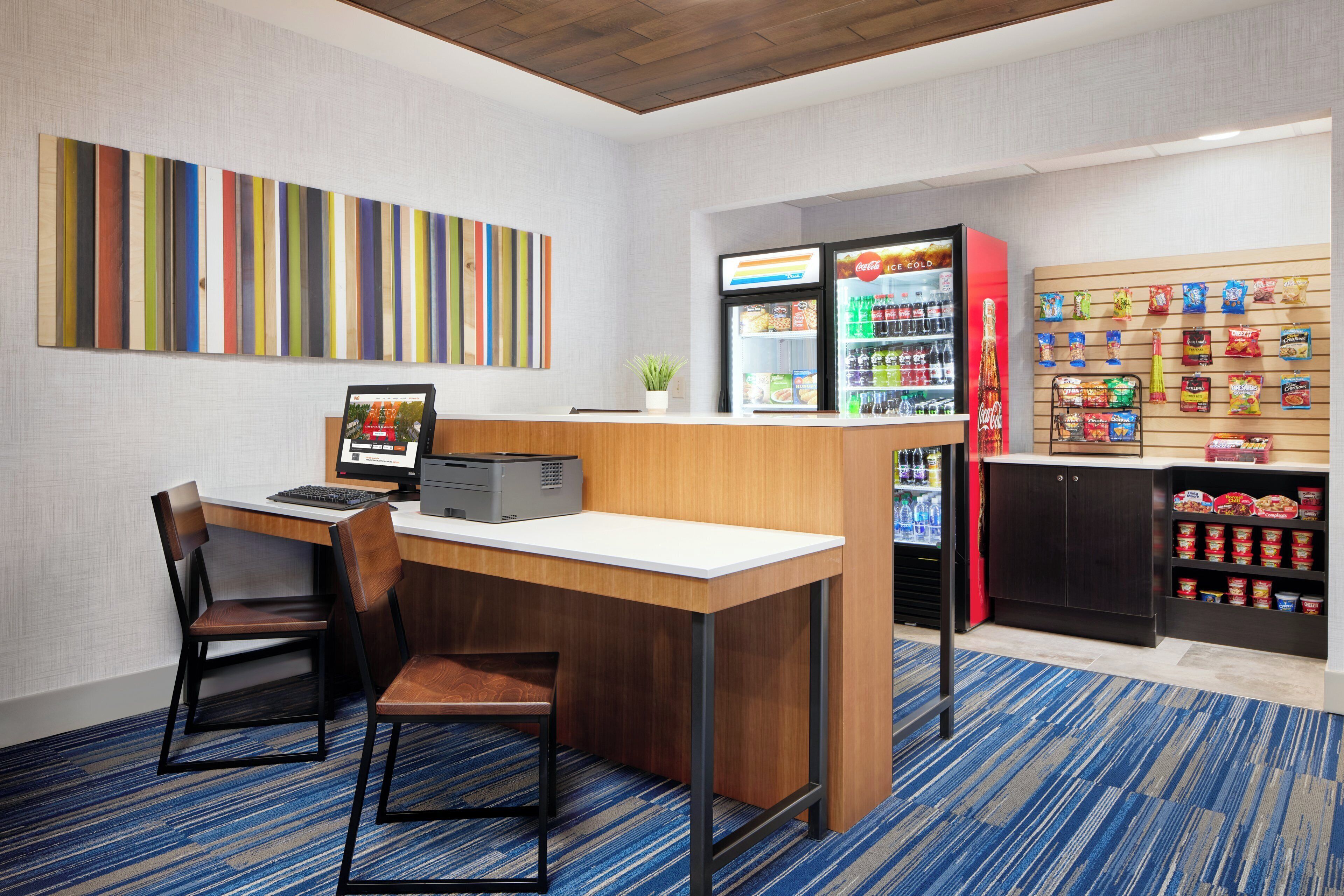 A hotel room with a desk, chairs, a vending machine, and a snack bar.