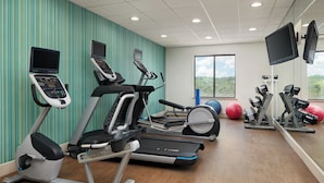 Une salle de sport équipée de tapis de course, de vélos elliptiques et de ballons d’exercice.