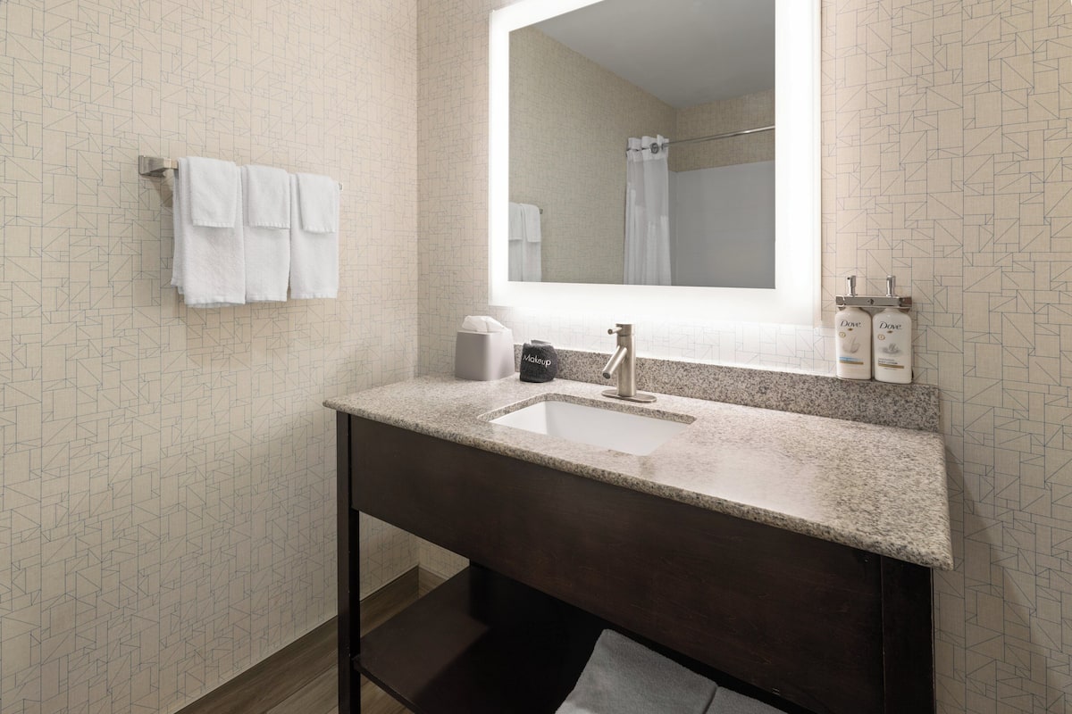 A bathroom with a sink, mirror, towel rack, and toiletries.