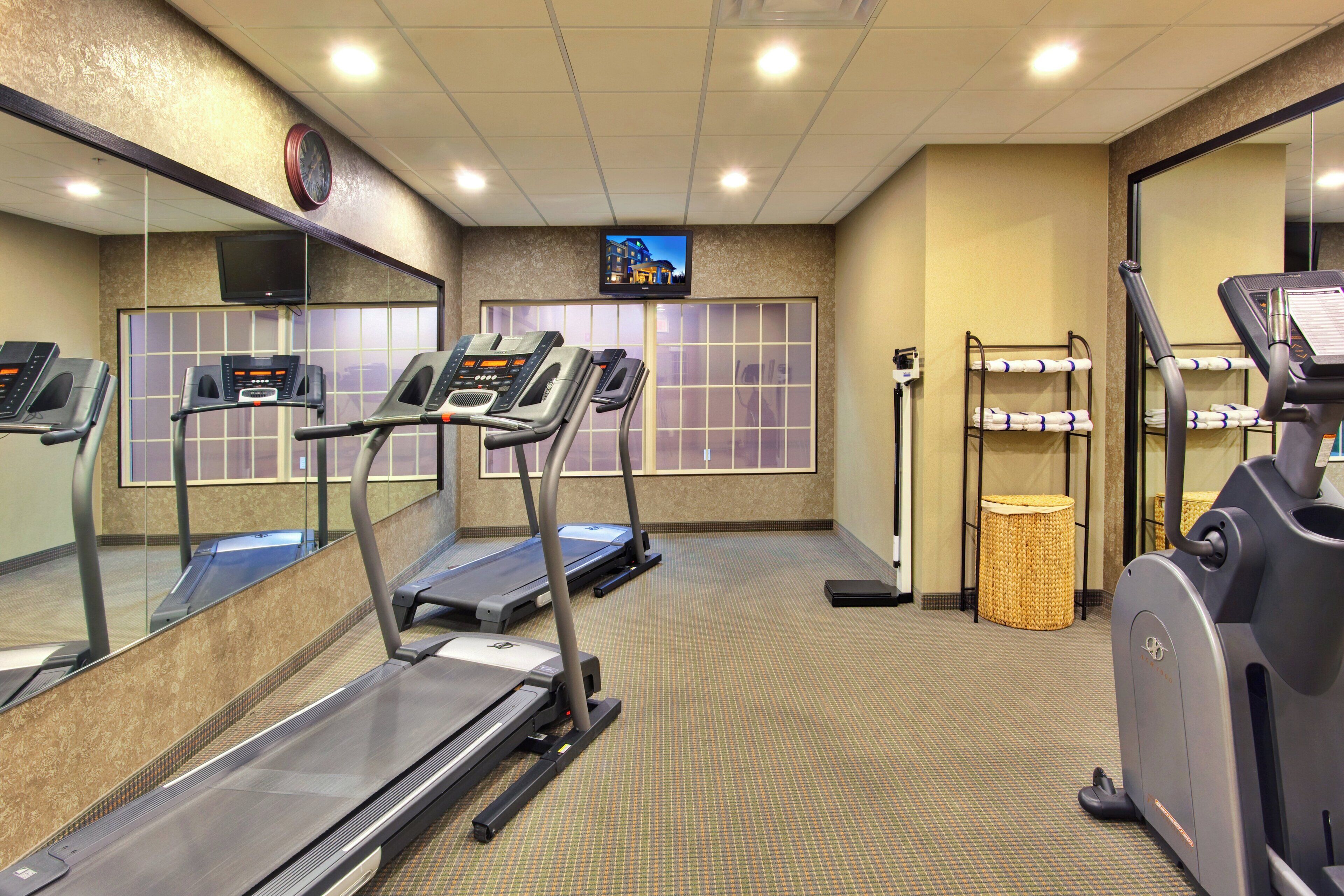 A fitness center with treadmills, a mirrored wall, a television, and a trash bin.