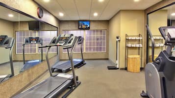 A fitness center with treadmills, a mirrored wall, a television, and a trash bin.