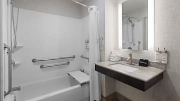 Un baño moderno con cabina de ducha, barras de apoyo, tocador con lavabo y espejo.