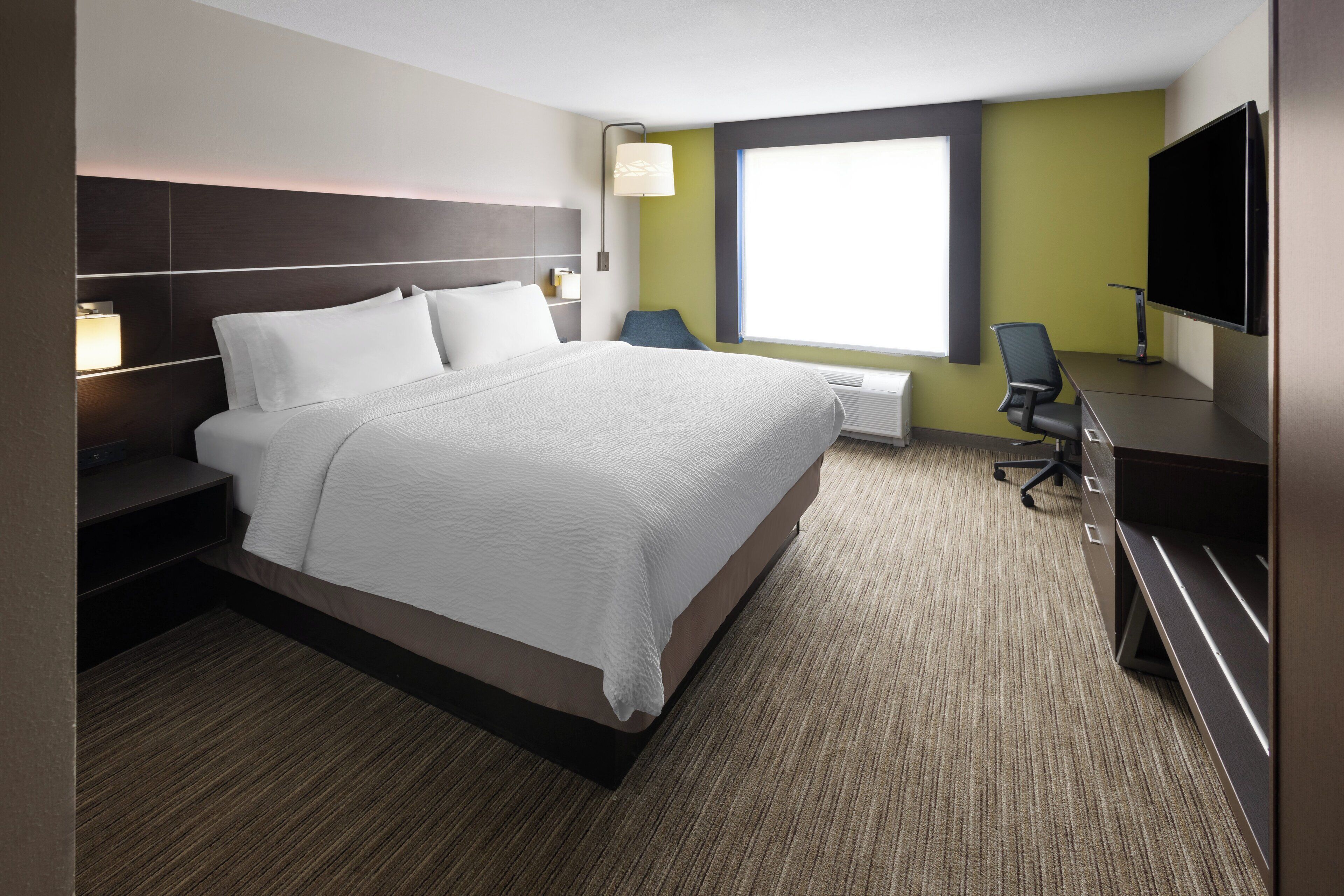 Habitación de hotel con una cama grande, un escritorio con silla, un televisor de pantalla plana y una ventana con persianas.