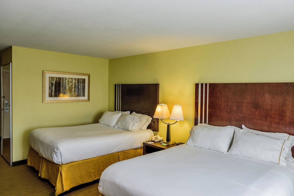 A hotel room with two single beds, a nightstand with a lamp, and a framed picture on the wall.
