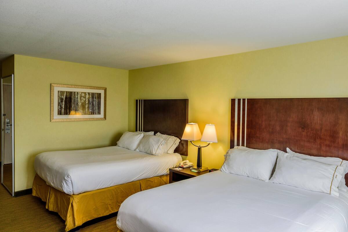 A hotel room with two beds, a nightstand with a lamp, and a framed picture on the wall.