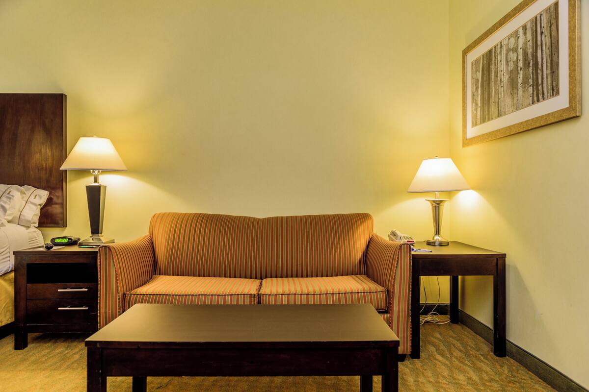 A hotel room with a striped sofa, two bedside tables with lamps, a wooden headboard, and a framed picture on the wall.