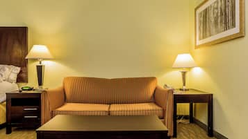A hotel room with a striped sofa, two bedside tables with lamps, a wooden headboard, and a framed picture on the wall.
