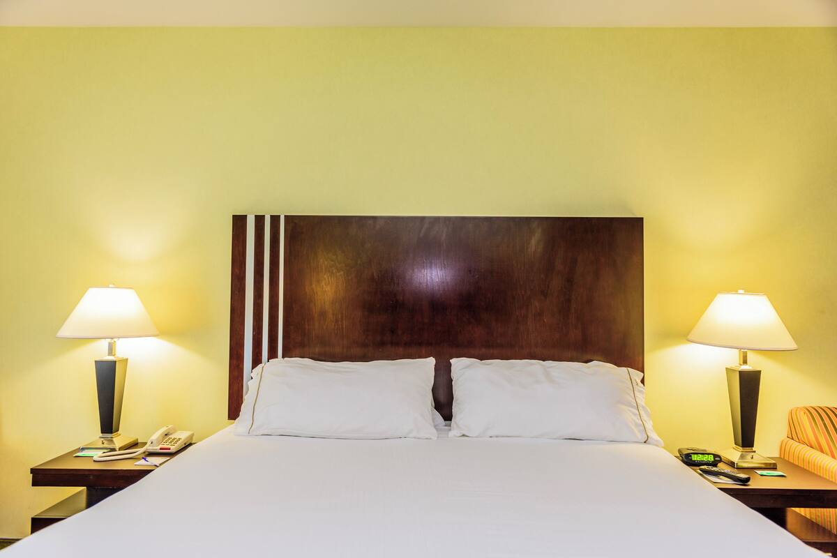 A hotel room with a large bed, two bedside tables with lamps, a telephone, and a clock.