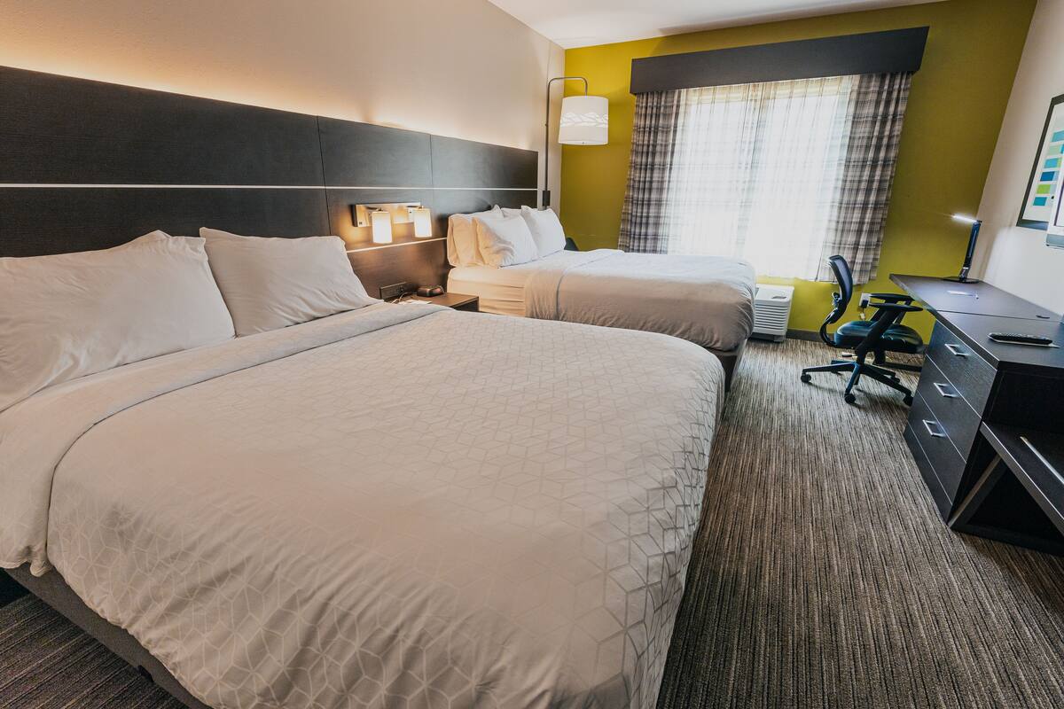 A hotel room with two beds, a desk, a chair, and a window with curtains.