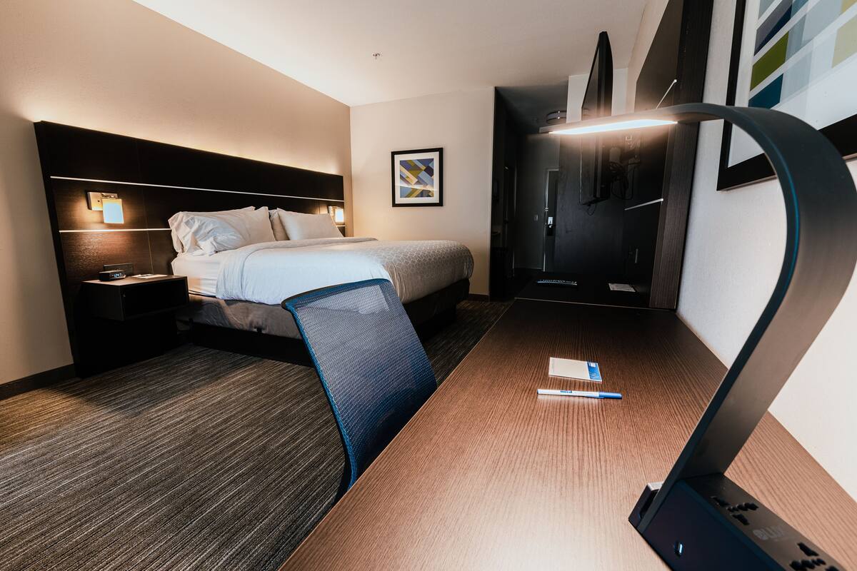 A hotel room with a bed, bedside table, desk with a laptop, and a chair.