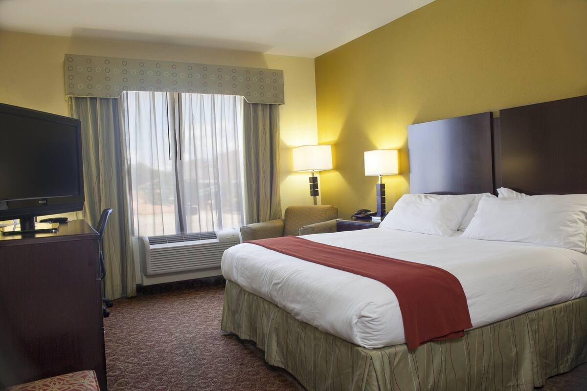 A hotel room with a bed, a desk, a chair, a television, and a window with curtains.