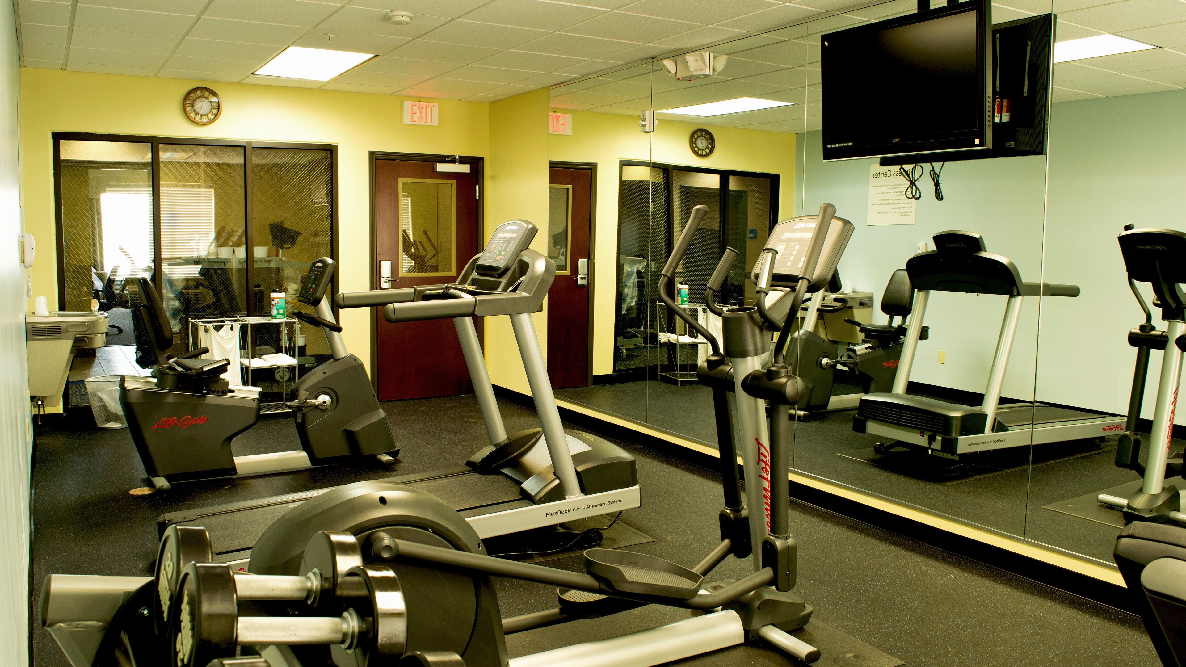 Une salle de sport équipée de divers appareils d’exercice, notamment des tapis de course, des vélos d’appartement et des appareils de musculation.