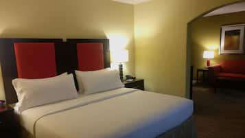 A hotel room with a large bed, a nightstand with a lamp, and a red armchair.