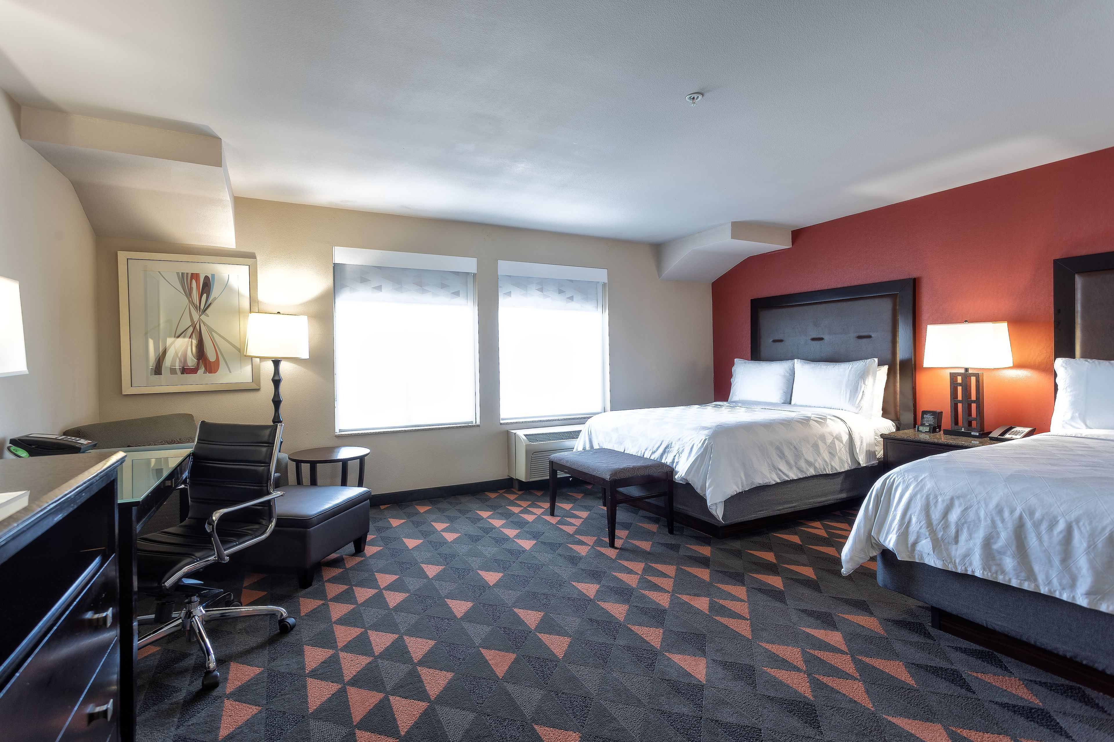 A hotel room with two beds, a desk, a chair, and a large window.
