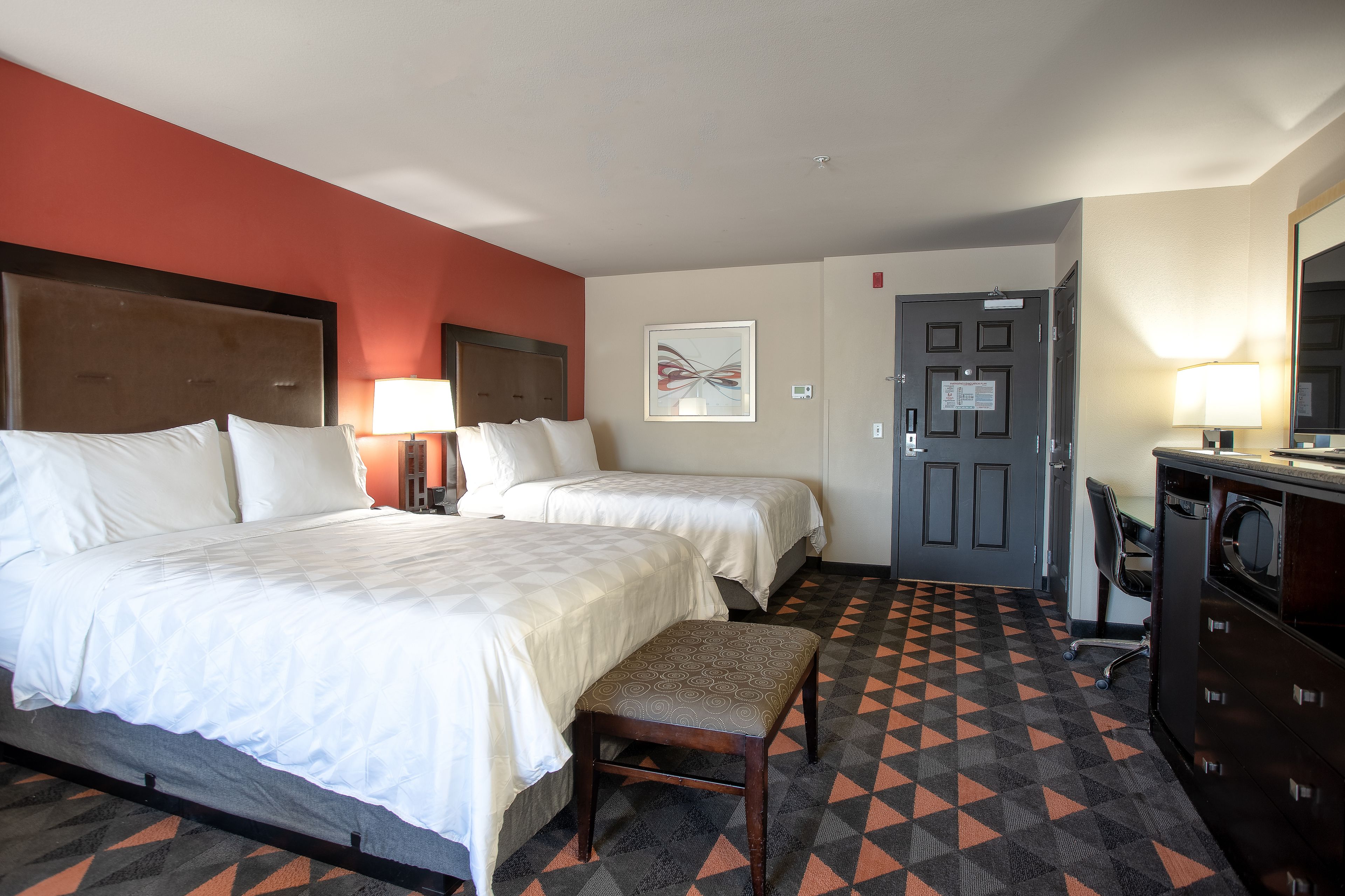 A hotel room with two beds, a desk, a chair, and a patterned floor.