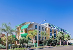 A multi-story hotel with a curved facade, outdoor seating area, and palm trees.