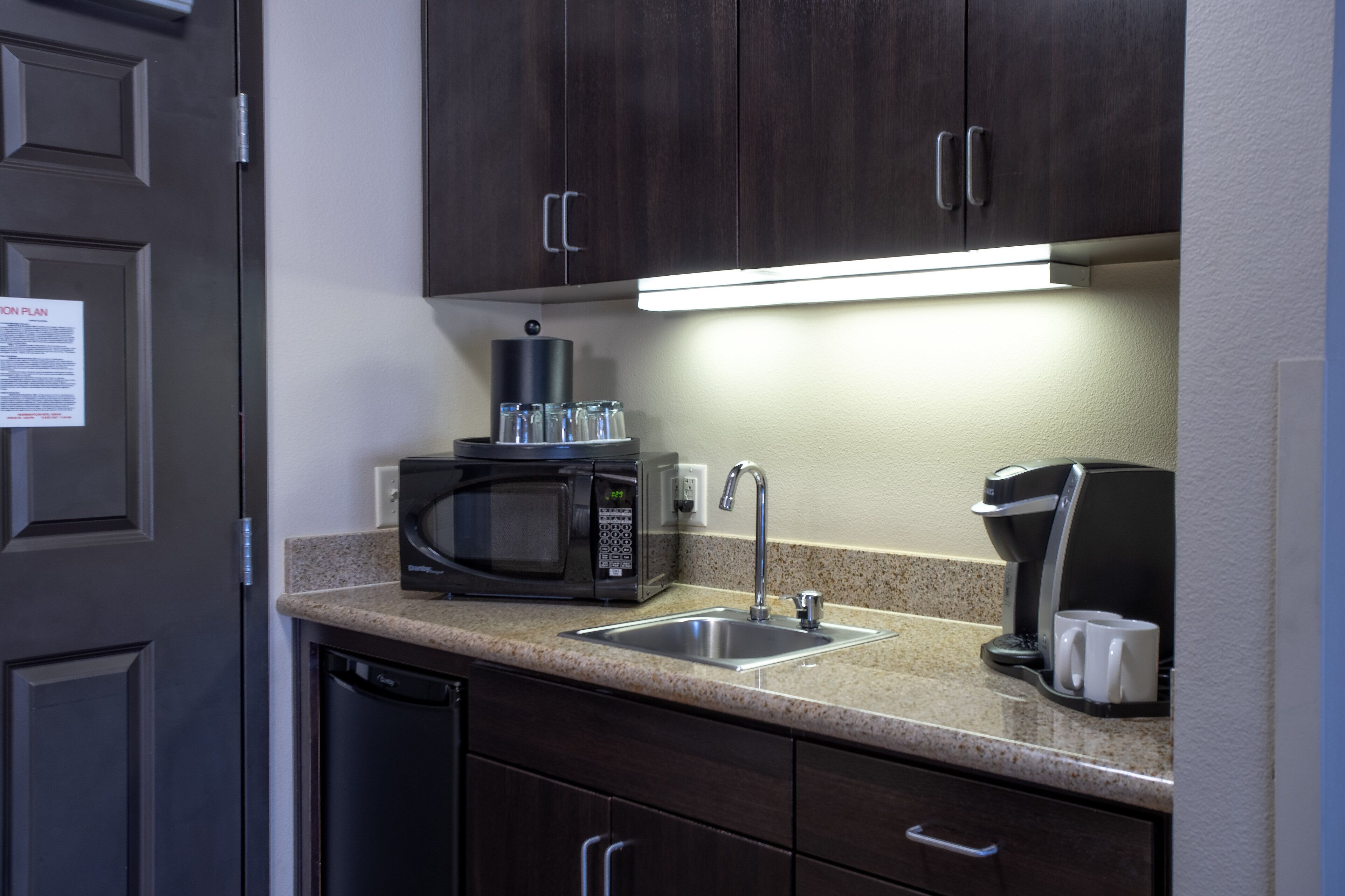Una cocina con microondas, cafetera y lavamanos.