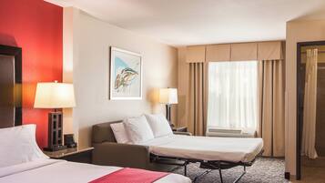 A hotel room with two beds, a desk, a chair, a lamp, a painting, and a window with curtains.