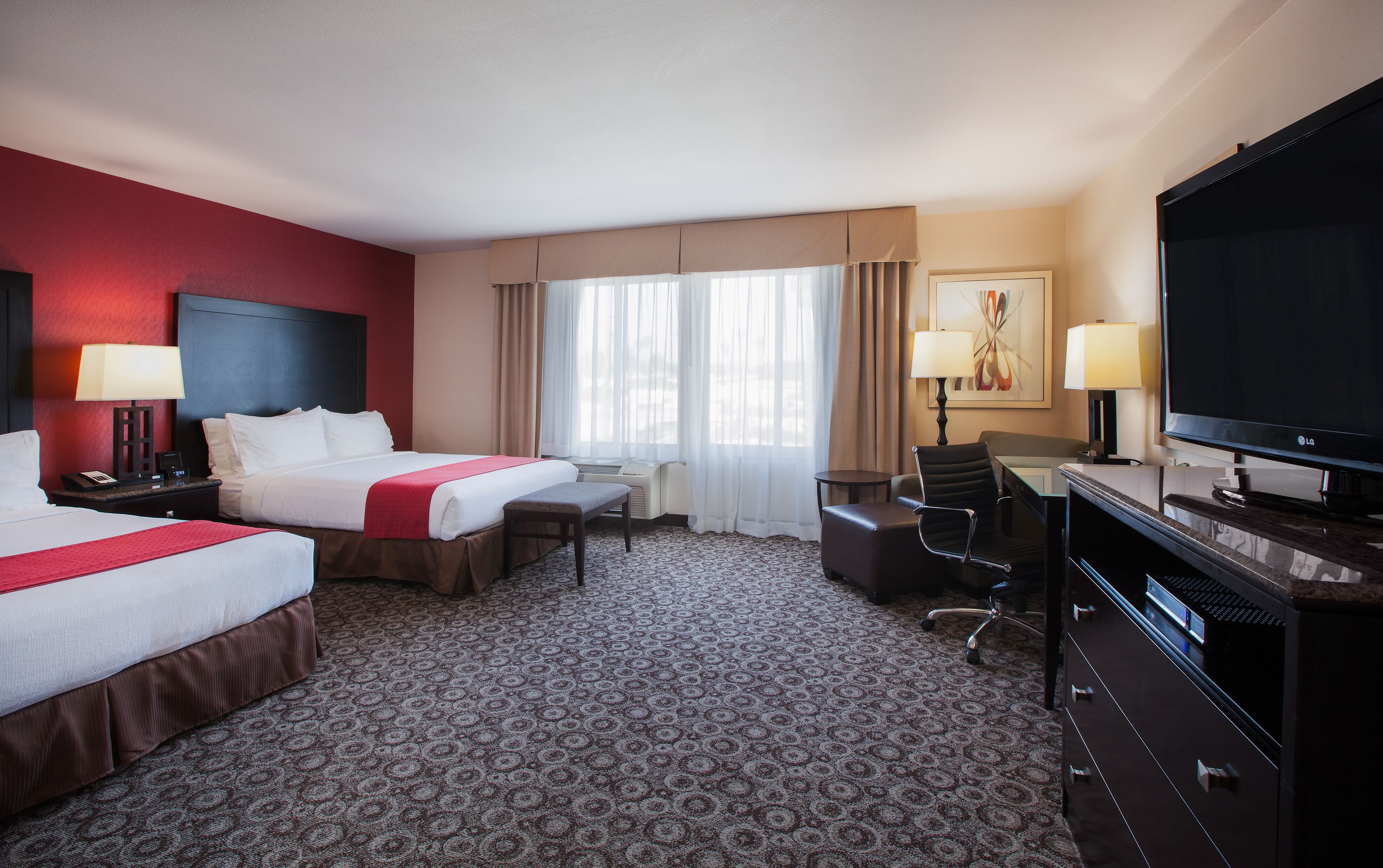 A hotel room with two beds, a desk, a chair, a television, and a painting on the wall.