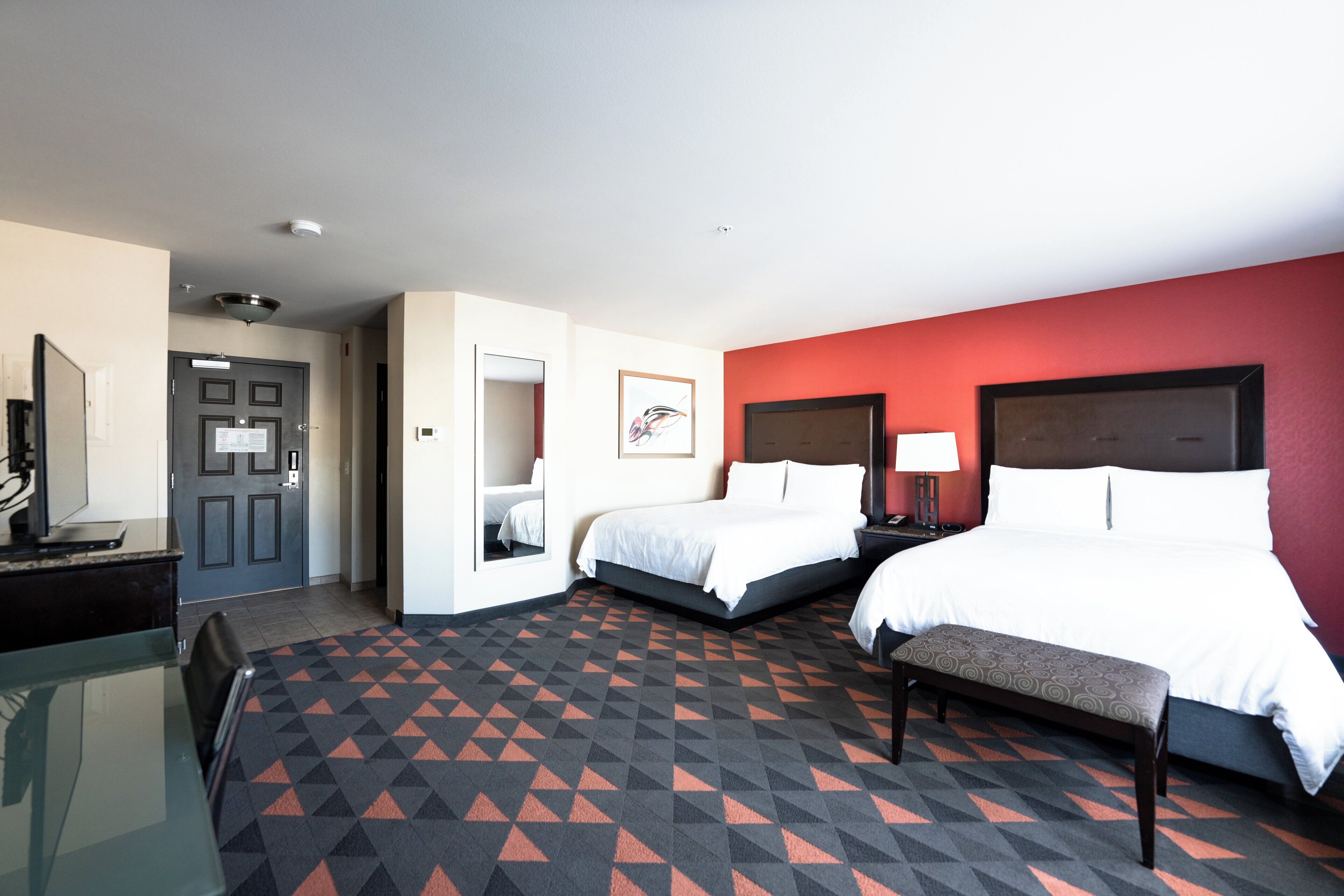 A hotel room with two beds, a desk, a chair, and a patterned carpet.