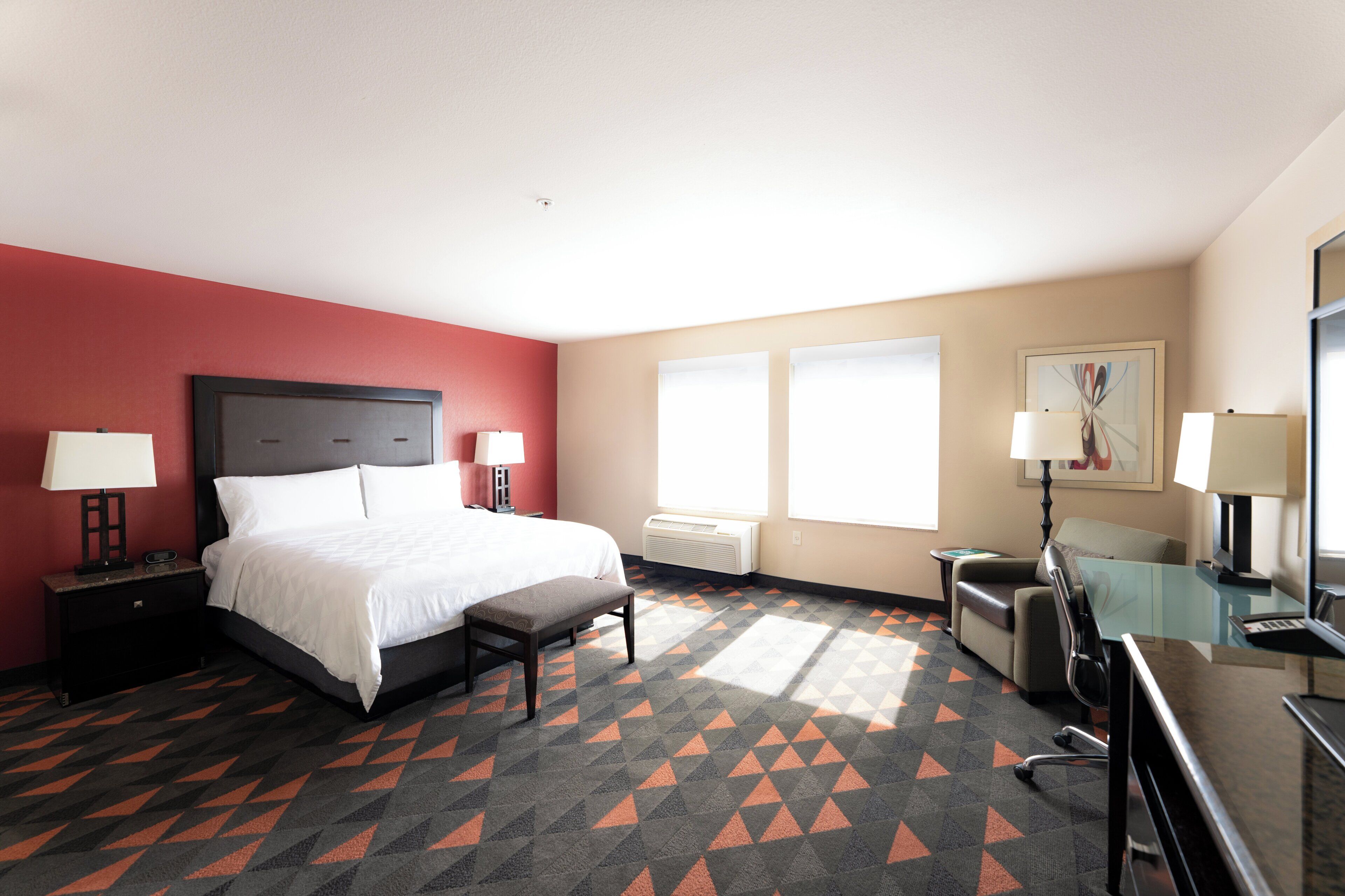 Una habitación de hotel con cama, escritorio, silla y un ventanal grande.