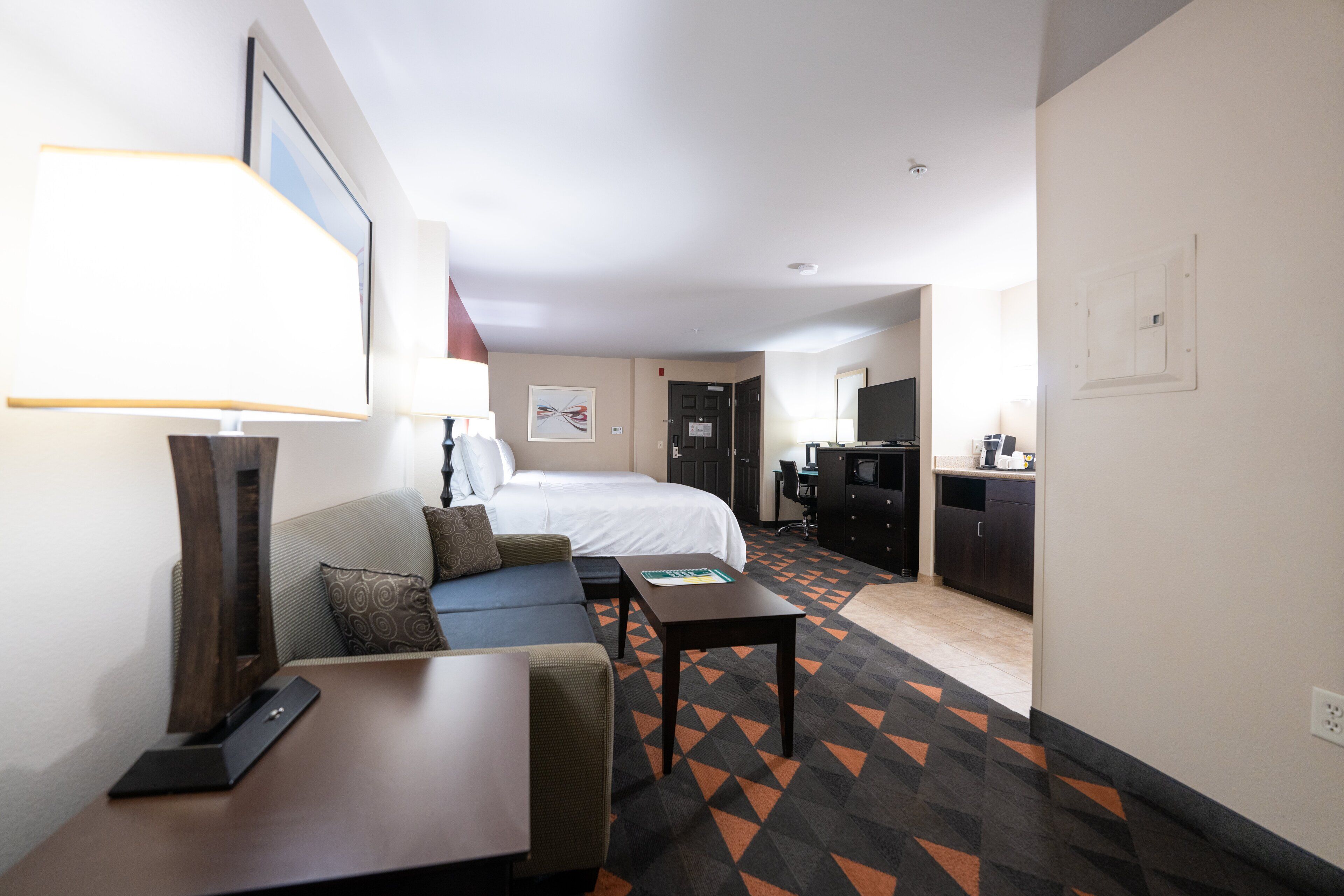 A hotel room with a bed, a sofa, a desk, and a kitchenette.