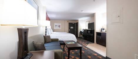 A hotel room with a bed, a sofa, a desk, and a kitchenette.