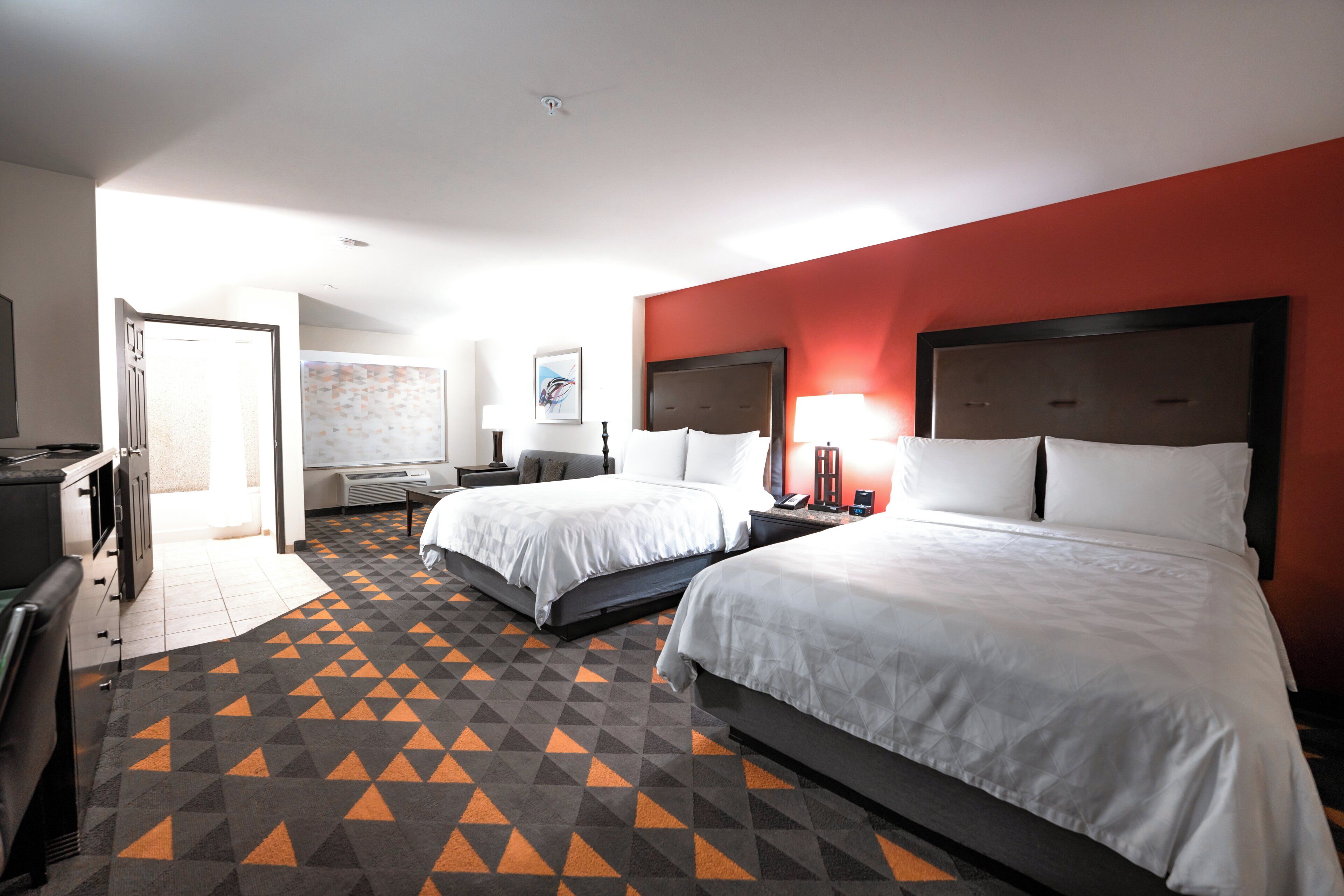 A hotel room with two beds, a desk, a chair, a TV, and a bathroom.