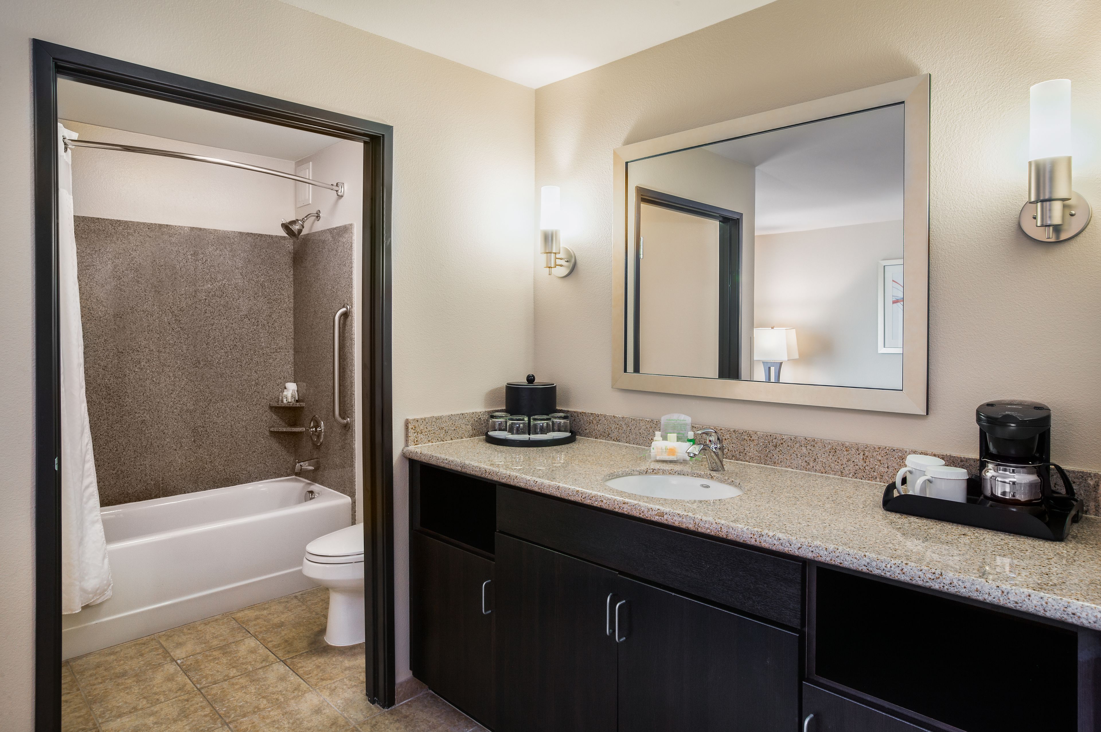 A bathroom with a bathtub, toilet, sink, and a coffee maker on the countertop.