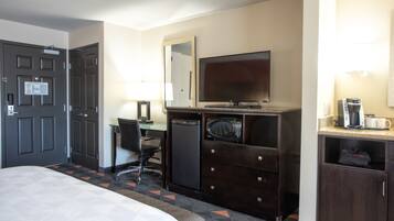 Een hotelkamer met een bed, een bureau met stoel, een televisie, een magnetron, een koffiezetapparaat en een minibar.