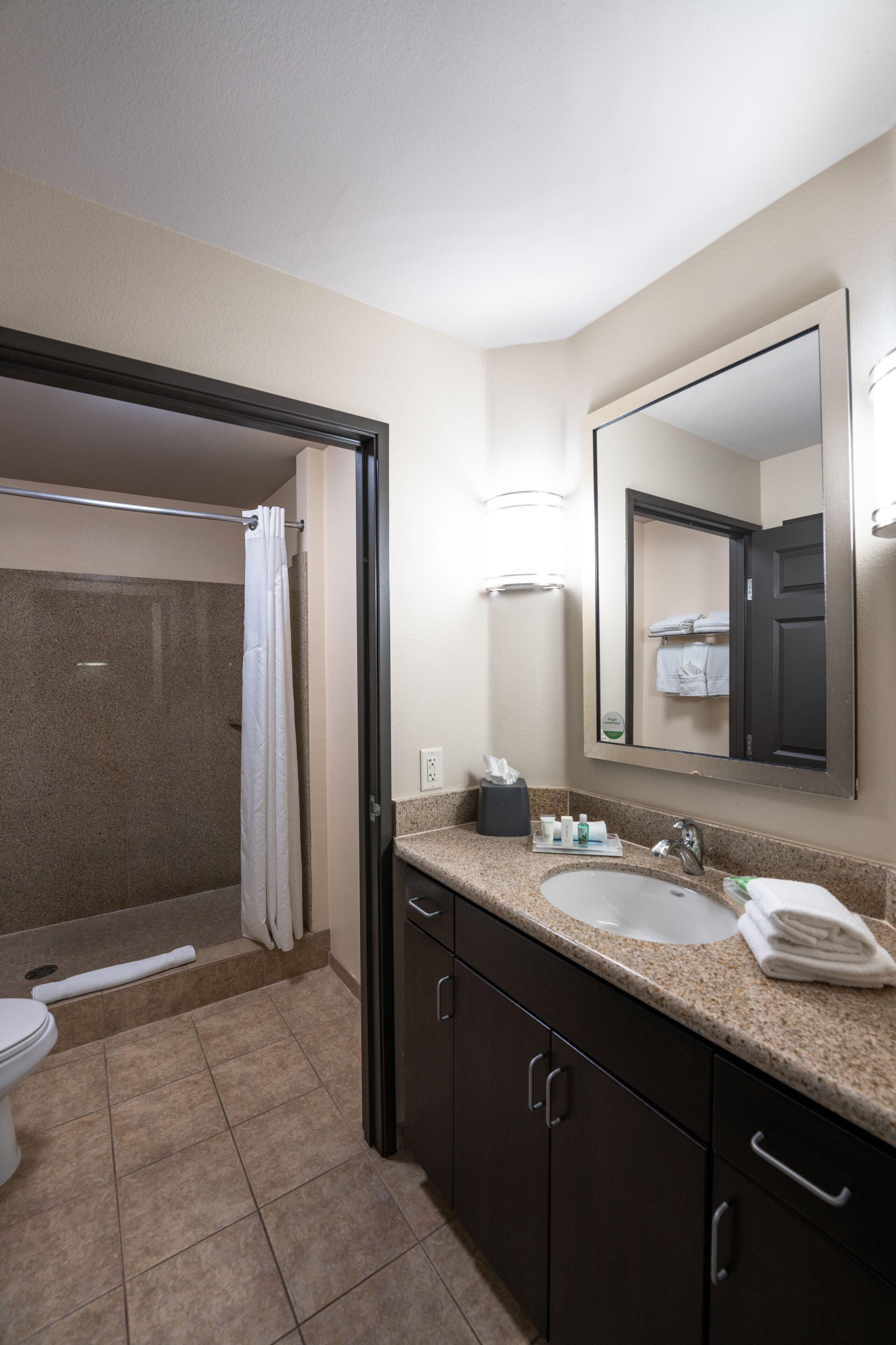 A bathroom with a shower, toilet, sink, and mirror.
