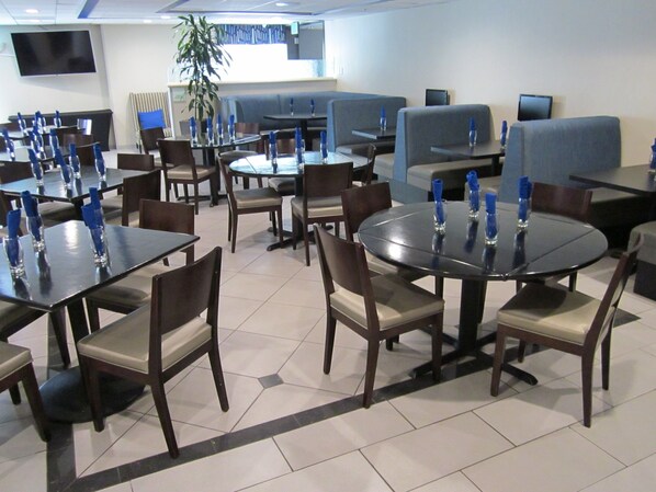 A restaurant with multiple tables and booths, some with blue napkins, and a flat-screen TV mounted on the wall.