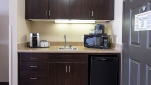 A compact kitchen with dark wood cabinets, a coffee maker, a microwave, and a dishwasher. - Holiday Inn Oceanside Camp Pendleton Area by IHG (Oceanside)