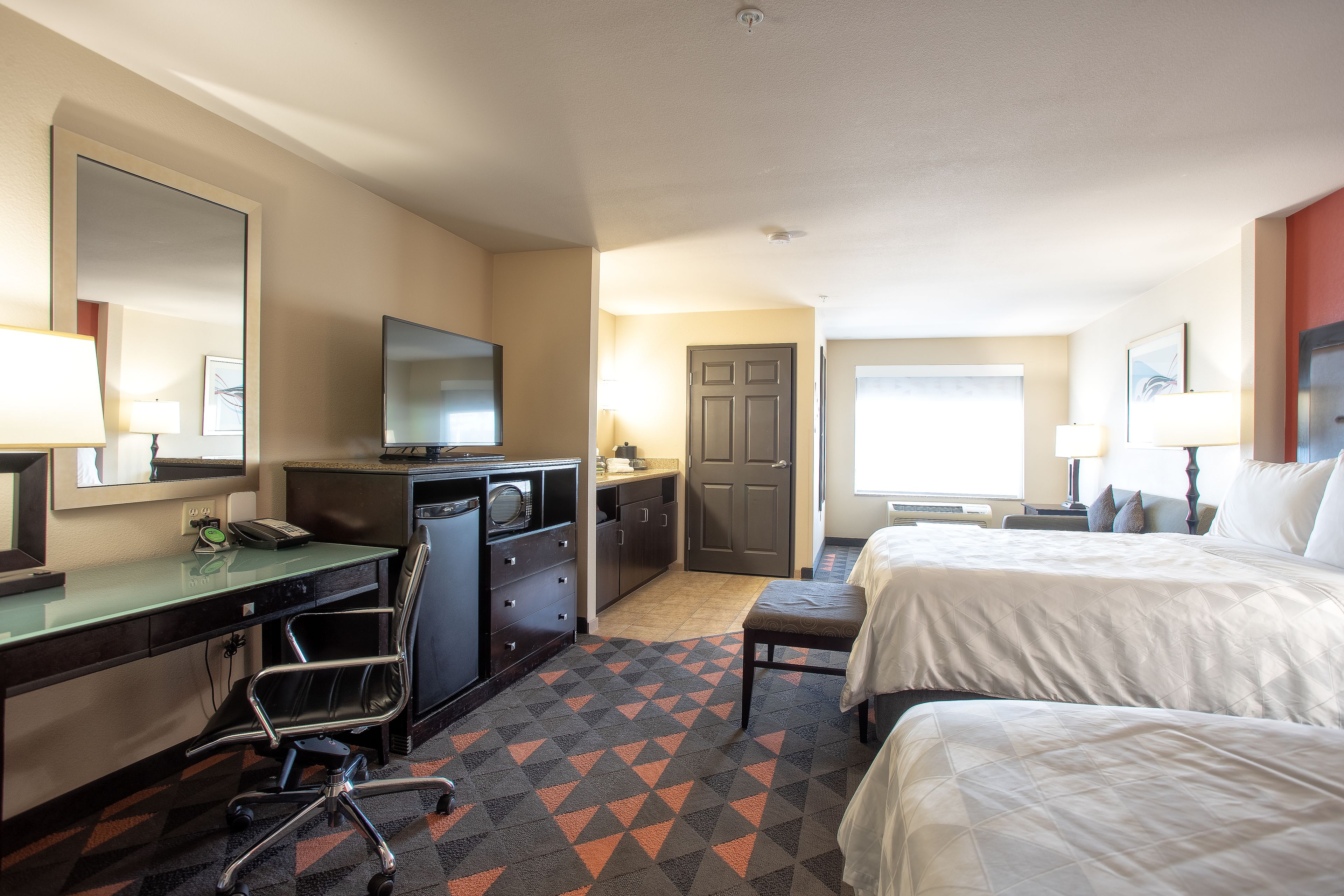 A hotel room with a desk, chair, bed, and a TV.