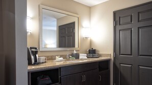 A modern bathroom with a dark wood vanity, a large mirror, and a coffee maker. - Holiday Inn Oceanside Camp Pendleton Area by IHG (Oceanside)