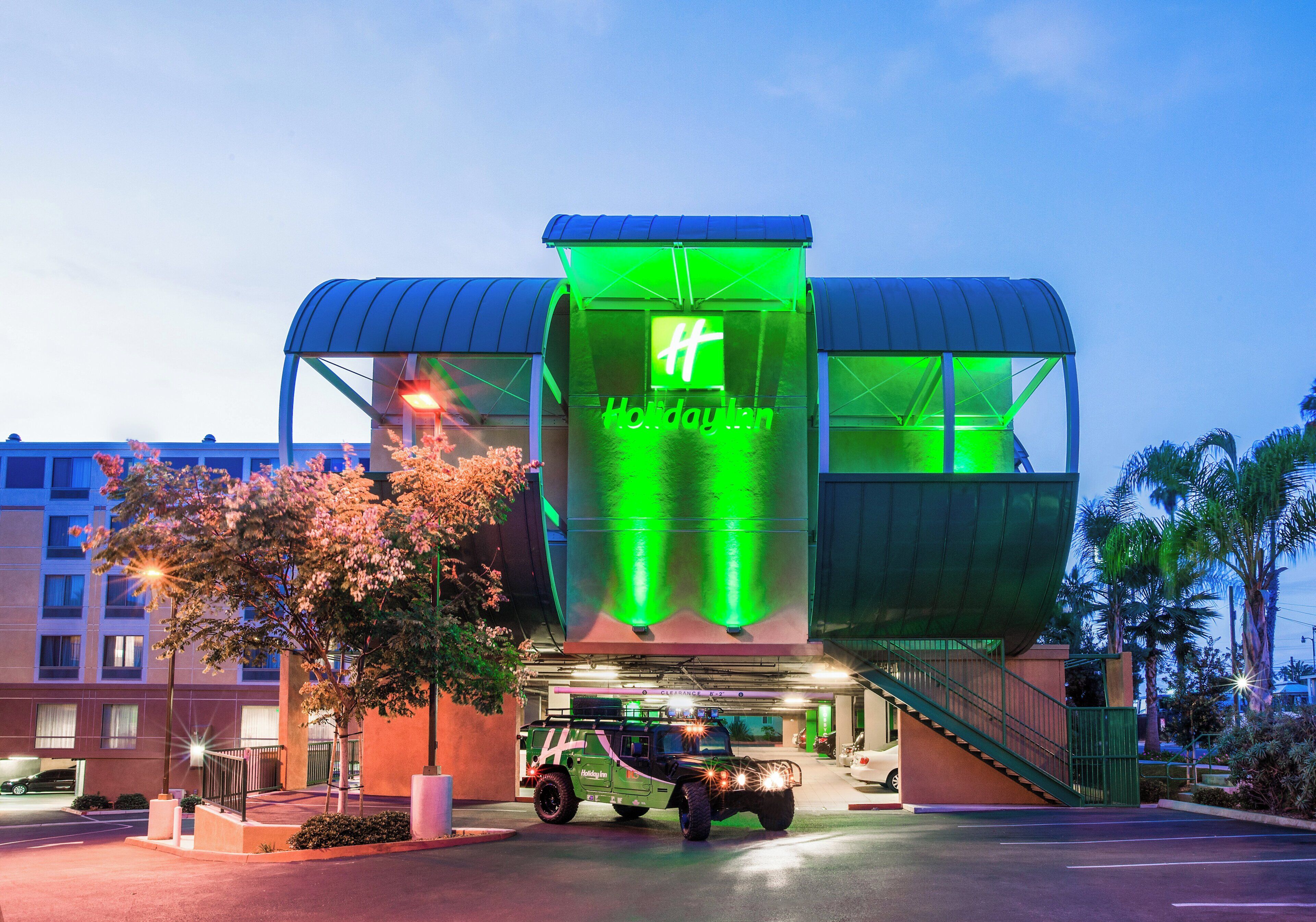 Un hotel Holiday Inn con un llamativo letrero de neón verde, un acceso cubierto y un estacionamiento con un vehículo.