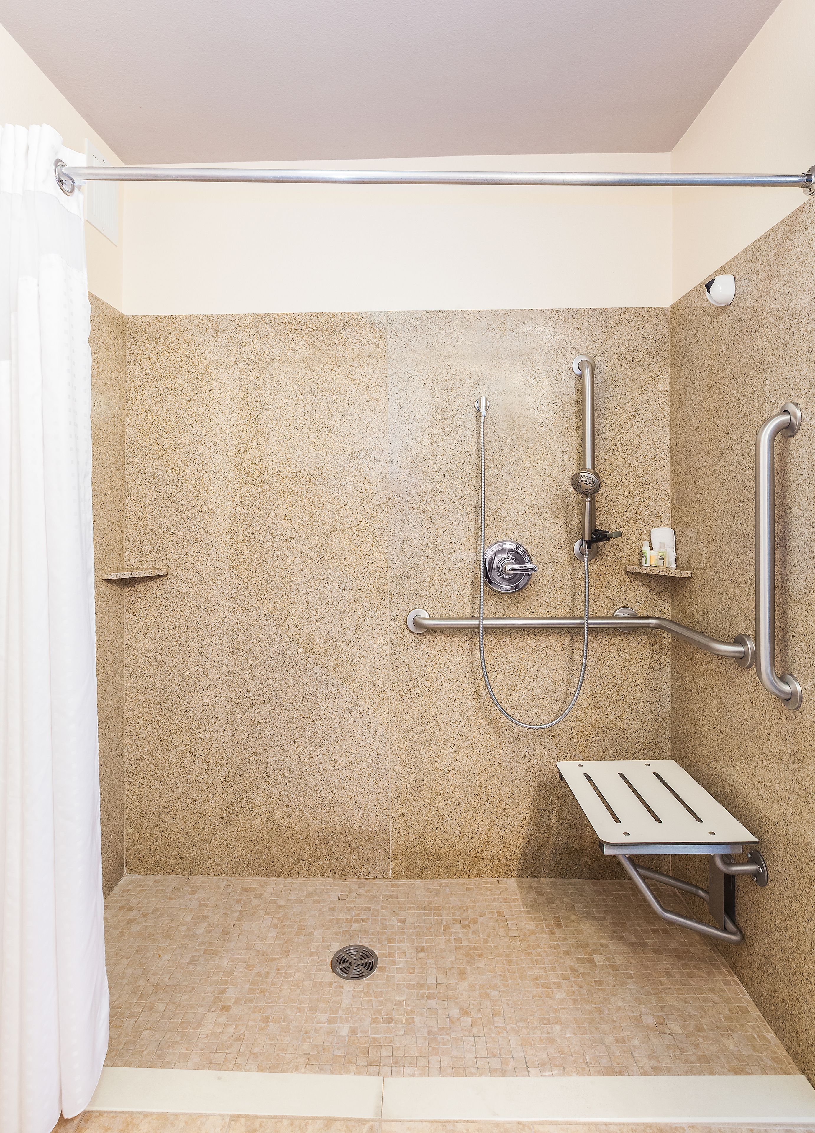 A shower area with a sloped floor, a grab bar, a handheld showerhead, and a handheld shower attachment.