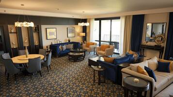 A modern hotel room with a round dining table, sofas, and a large window with curtains.