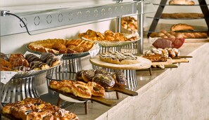 Un bufé con diversas opciones de pastelería y productos horneados exhibidos en soportes metálicos.
