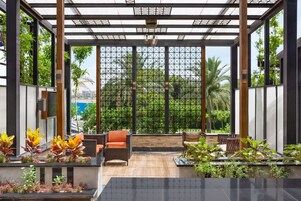 Un espacio de estar al aire libre con techo, mobiliario de mimbre y plantas en macetas.