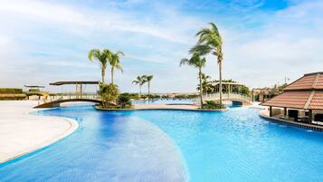 Relax by the pool surrounded by palm trees and a covered seating area, with a bridge leading to the adjacent beach.