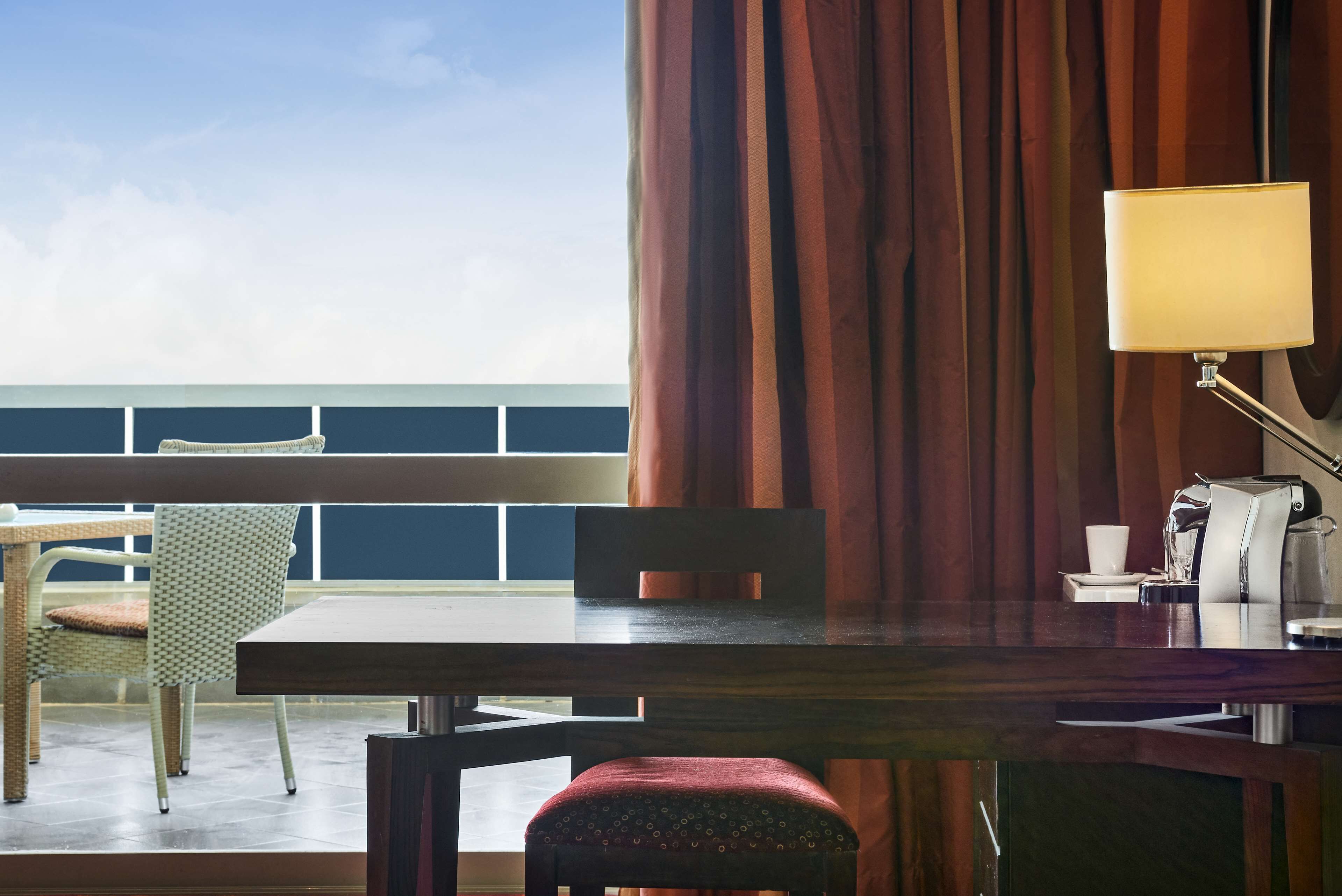 A dining area with a table, chairs, a lamp, and a view of the sea.
