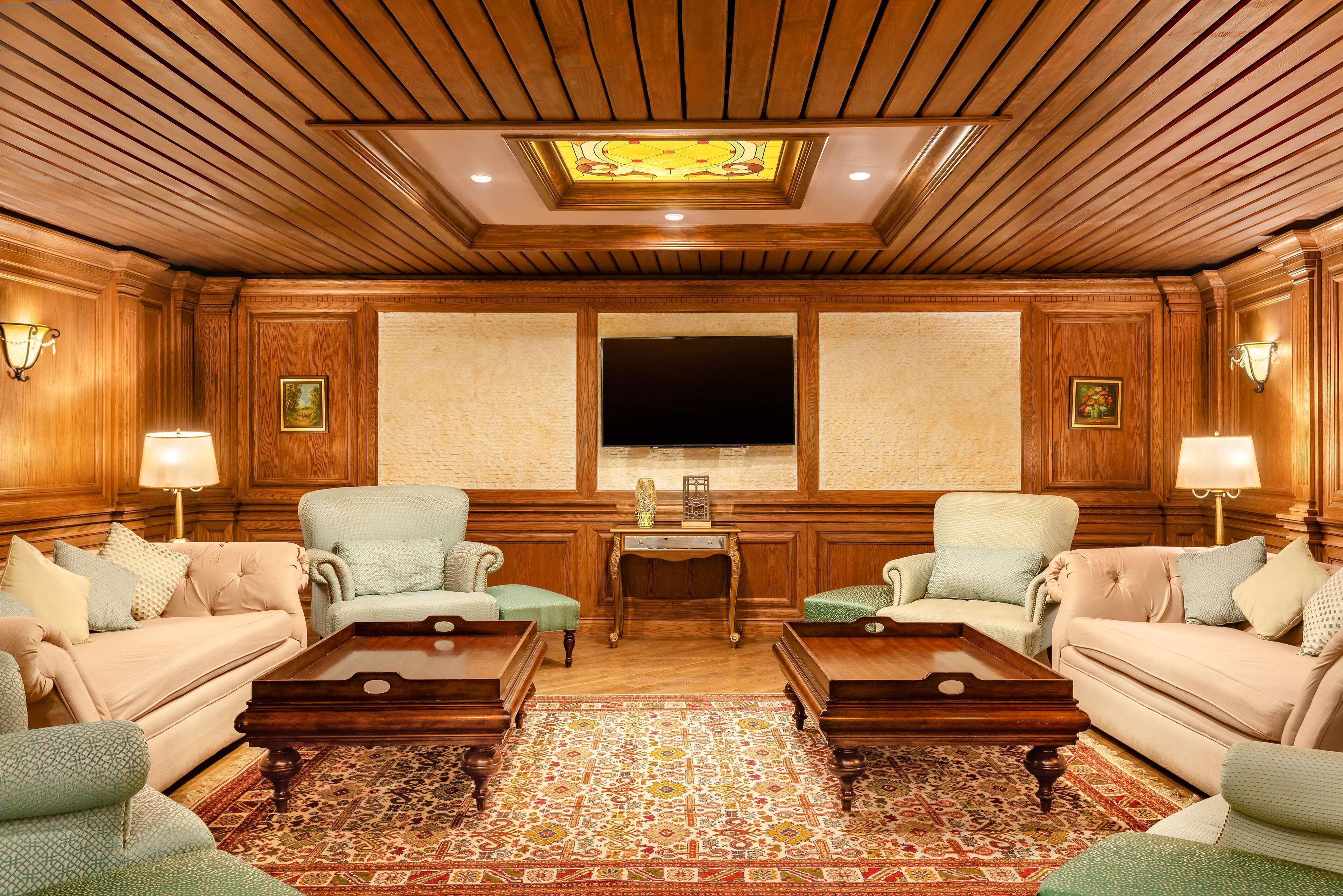 A room with wooden paneling, a large flat-screen TV, two armchairs, a sofa, and a patterned rug.