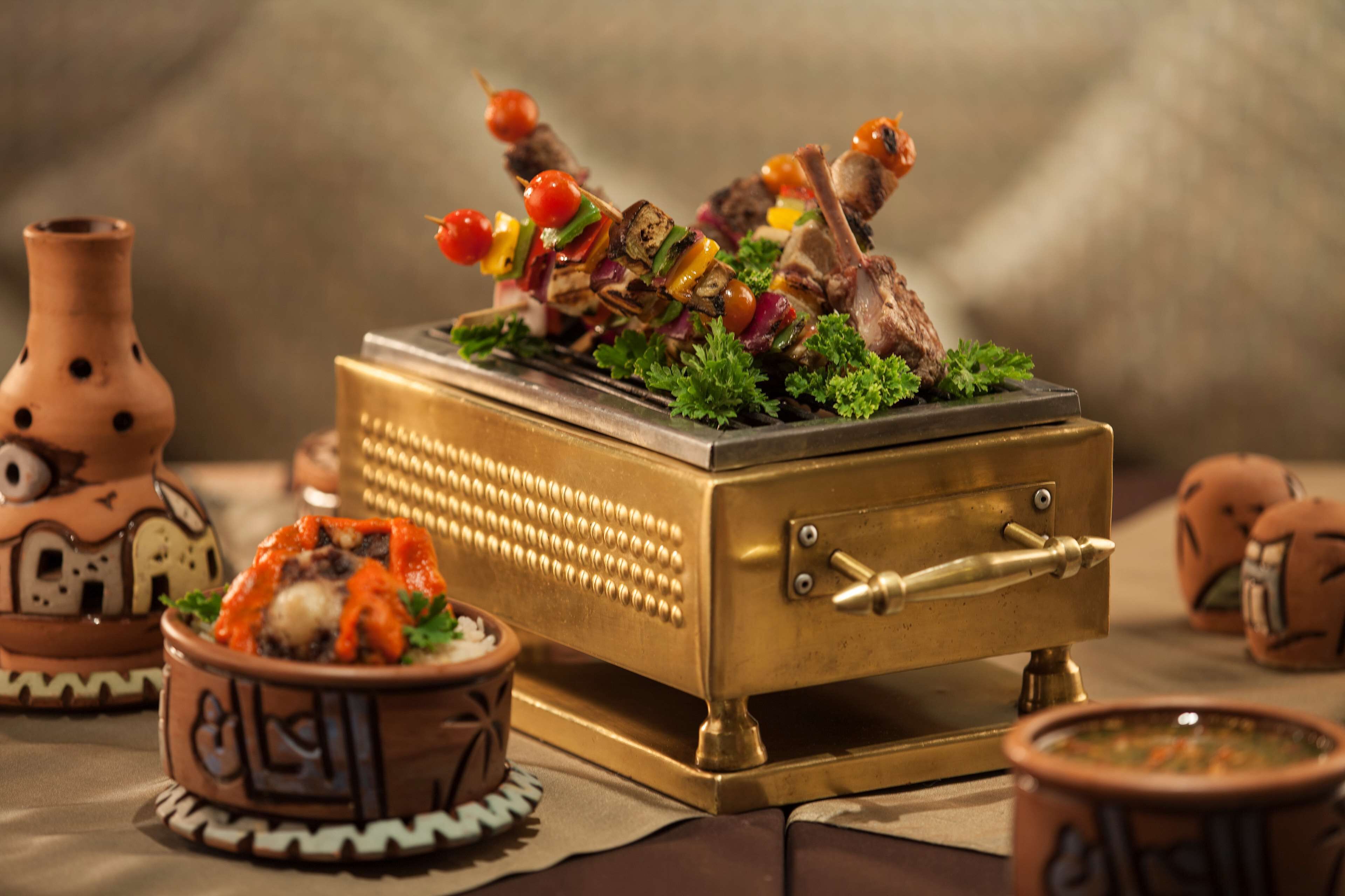 Messinkinen arkku, jonka päällä on vartaita ja kulho salaattia, ja sen ympärillä on saviruukkuja ja koristeellinen maljakko.