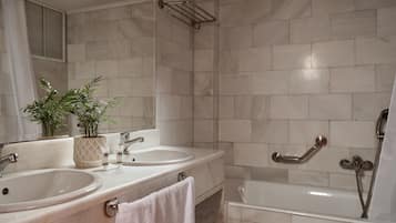 A bathroom with two sinks, a bathtub, and a shower. There are plants on the counter and a towel hanging on the wall.