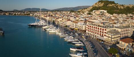 Un puerto deportivo con barcos amarrados a lo largo de la costa, junto a una zona urbana densamente construida con edificios y un paisaje montañoso de fondo.