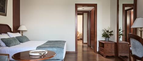 Una habitación de hotel con cama, una mesa redonda de madera, una silla, un sofá, un espejo y una planta en maceta.